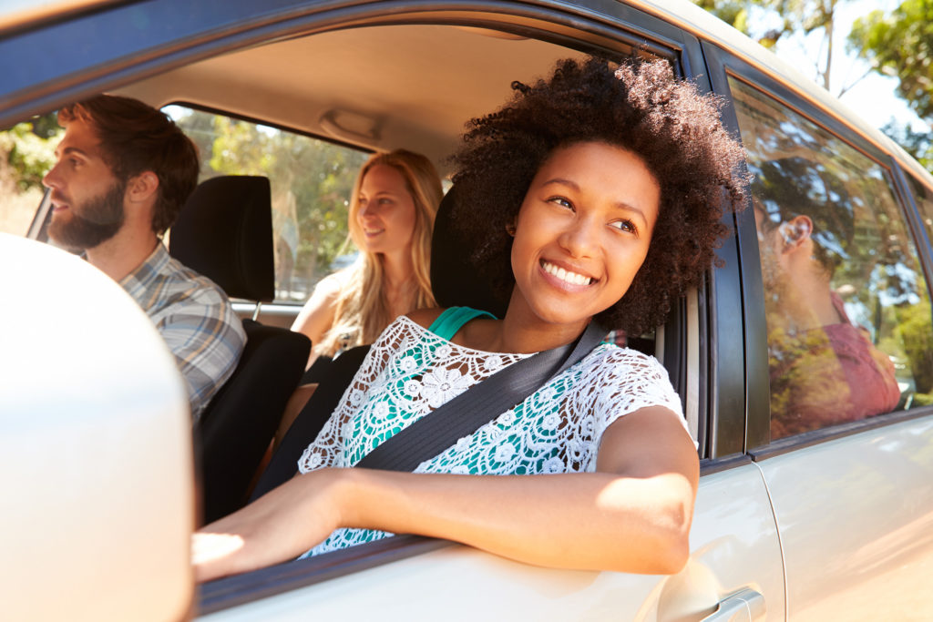 Young adults riding in a car with the focus on a pretty young girl leaning out the car window