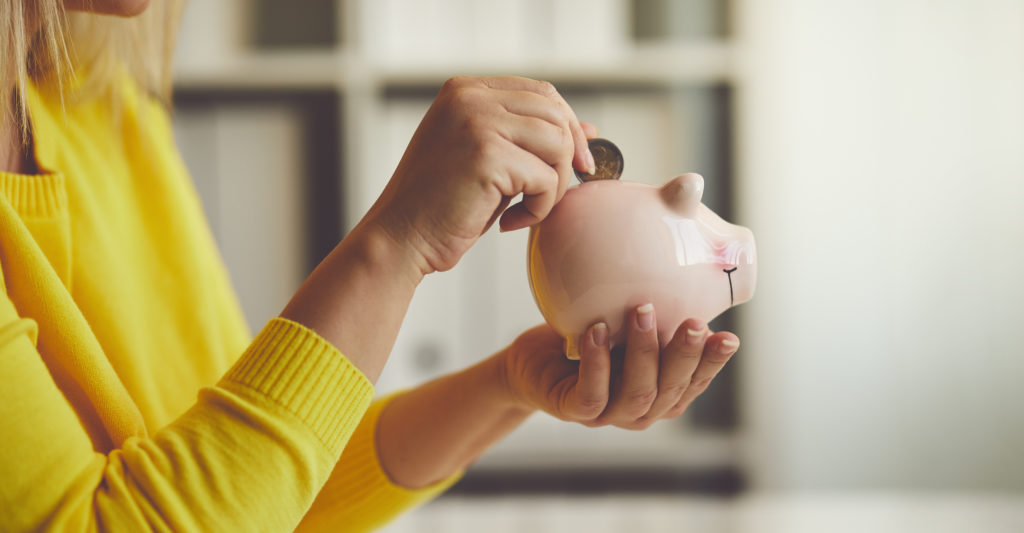 Woman inserts a coin into her savings piggy bank