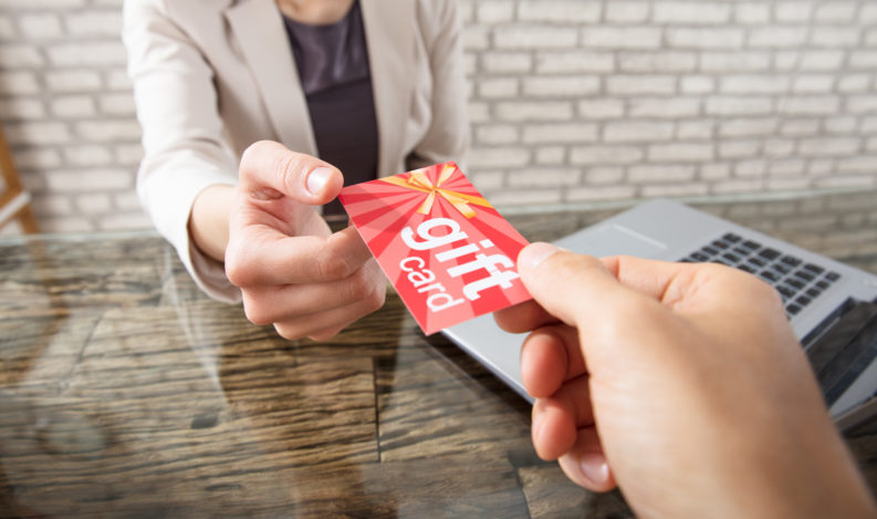 Close-up Of A Person Giving Gift Card To Businesswoman At Workplace In Office