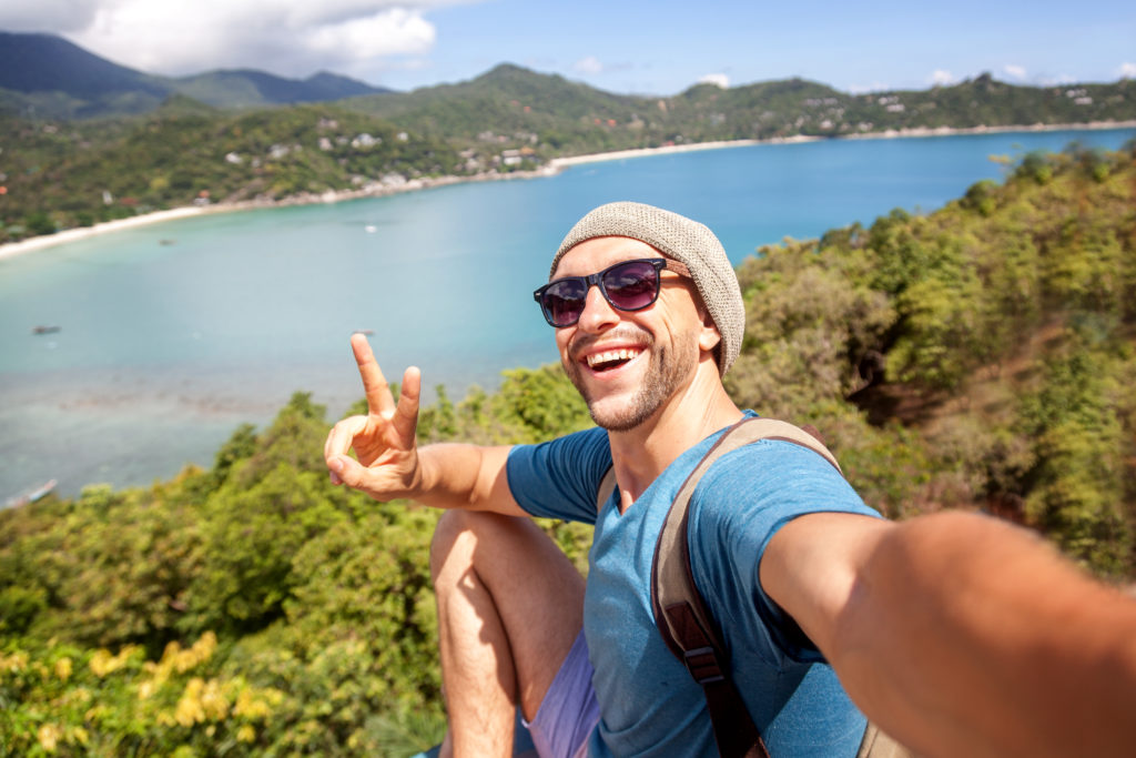 Young male hipster traveler doing selfie overlooking the tropical sea.
