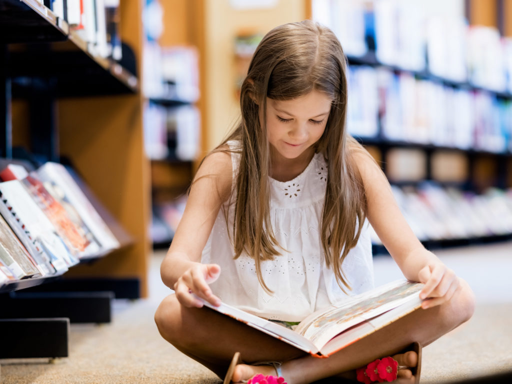 Little girl sitting on the floor and reading books in library
