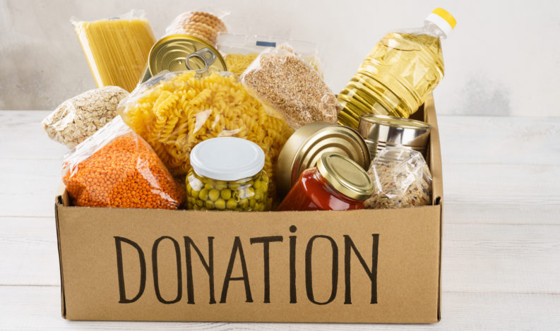 Donation box with various food. Open cardboard box with oil, canned food, cereals and pasta.