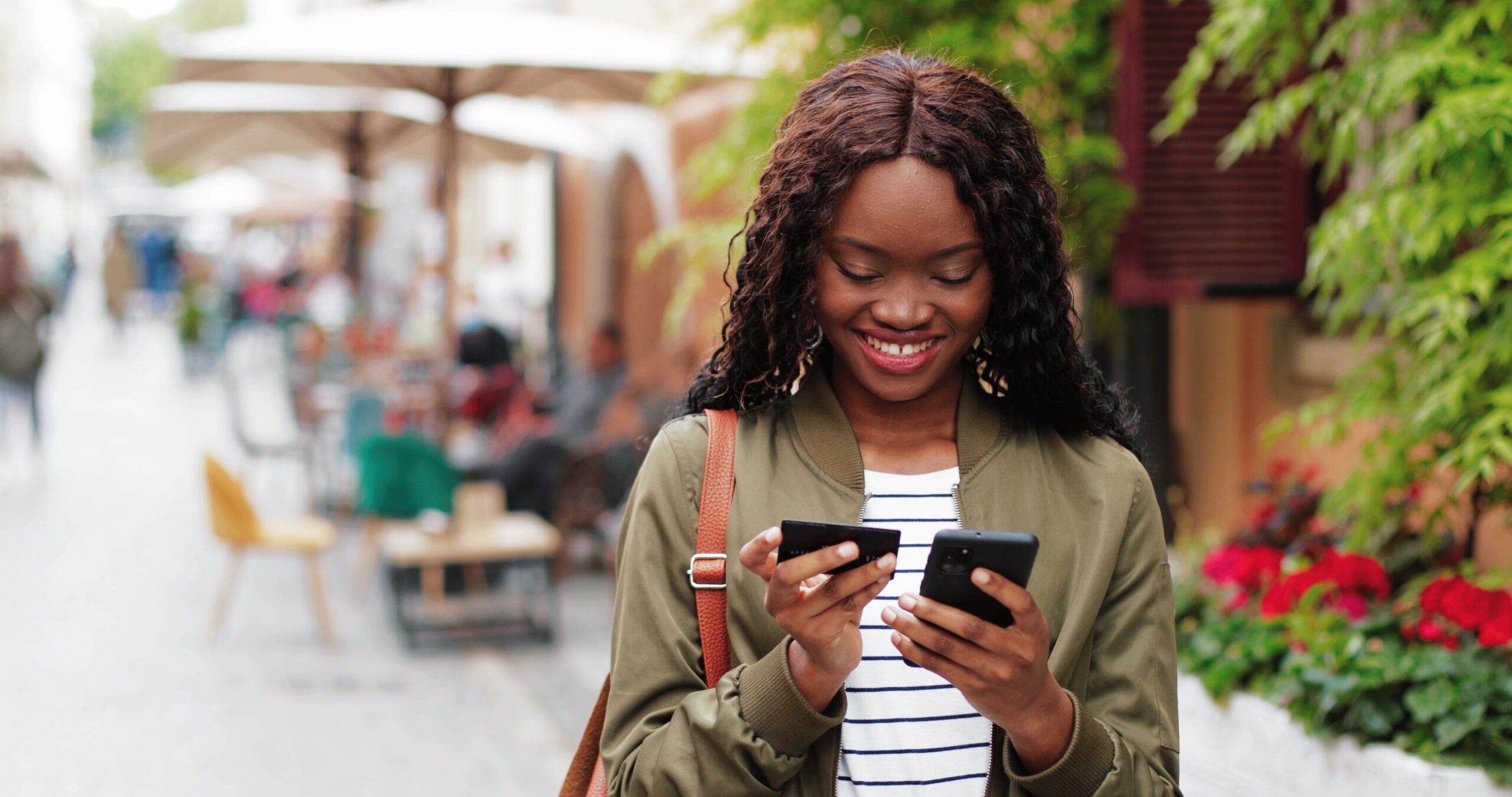 Online shopping. Waist up portrait view of African American woman holding credit card and typing details at her smartphone while having online shopping at the street
