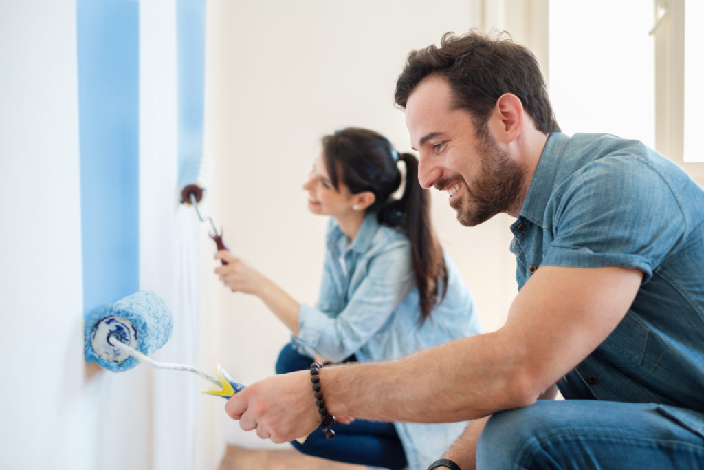 Young couple painting walls in their new house, do it yourself concept