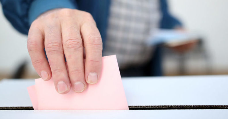 Man casts his ballot for the Board of Directors as he votes for the local elections at a polling station. Focus on hand.