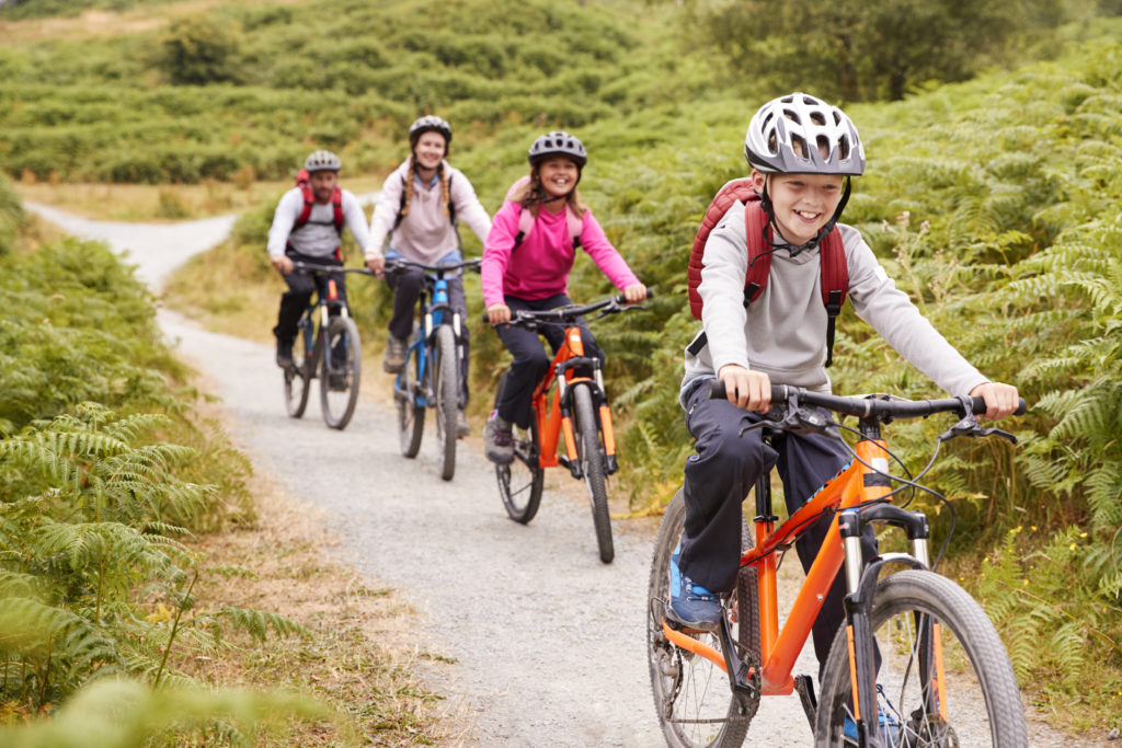 Pre-teen boy riding mountain bike with his sister and parents during a family camping trip, close up