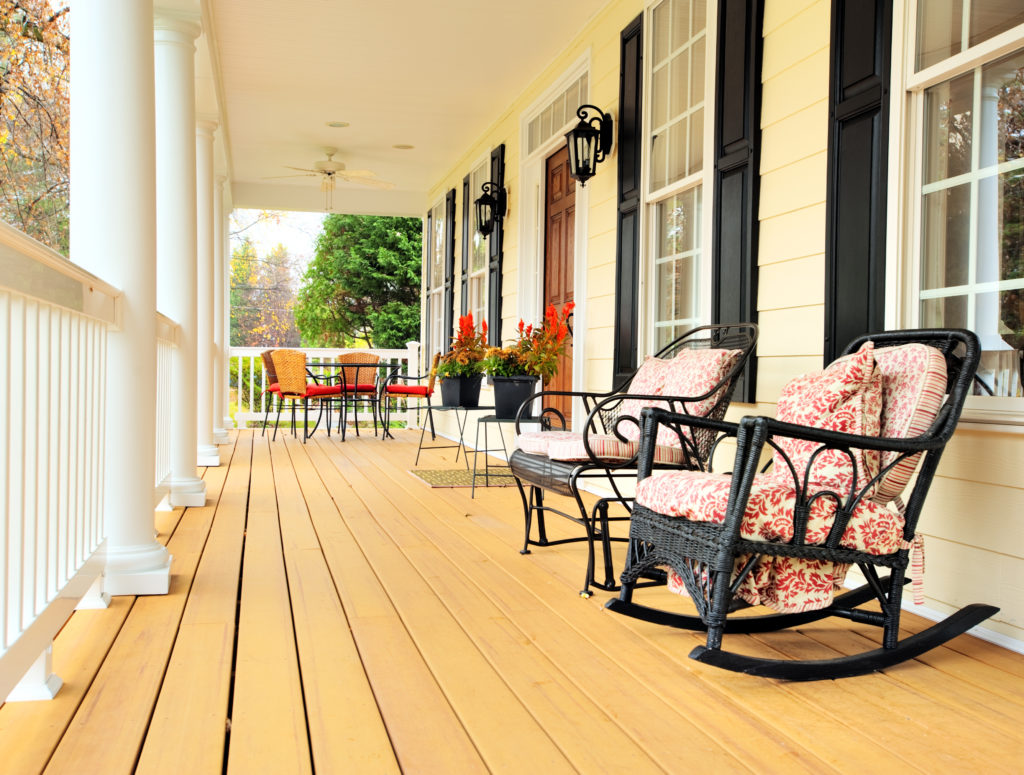 Low angle view of a large front porch with furniture and potted plants. Vertical format.