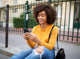 smiling african american young woman looking at cellphone in city