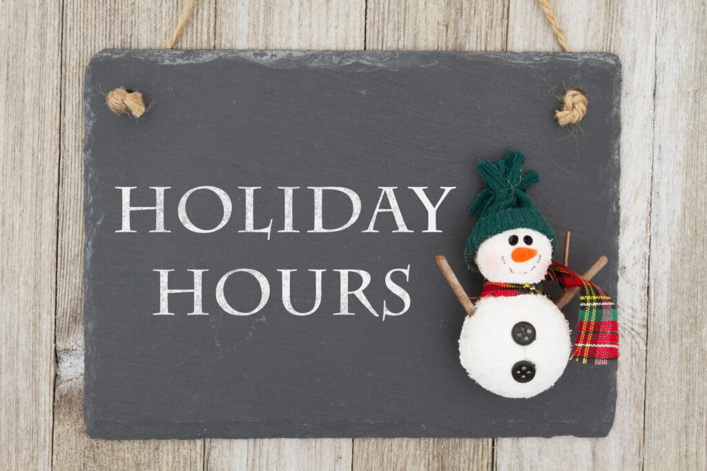 Old fashion Christmas store message, A retro chalkboard with a snowman hanging on weathered wood background with text Holiday Hours